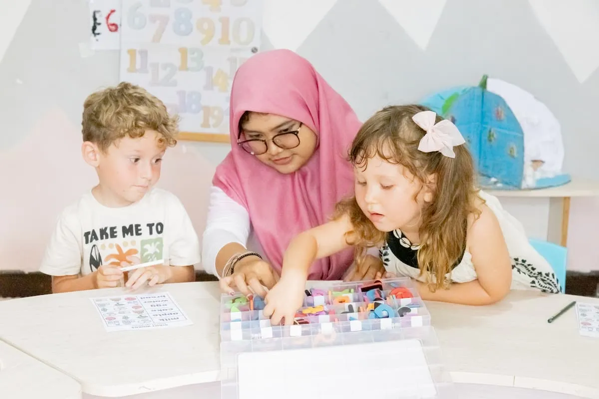 A teacher and two children sorting colourful letters at a table